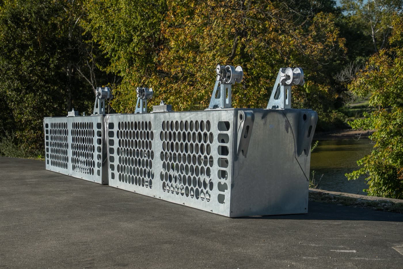 Two galvanized WaveBaffle sections with perforated baffle panels and lifting points, staged side by side on pavement beside the lake